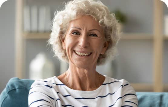 An older woman sitting on a couch smiling.