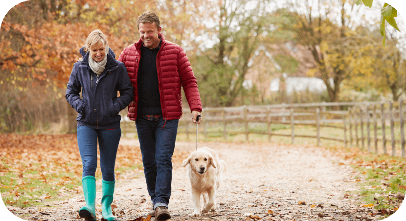 A couple is walking with their dog smiling.