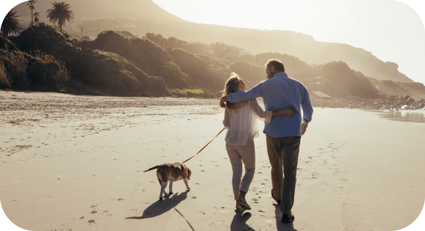 Couple walking on the beach with a dog and after reviewing their health insurance plan.
